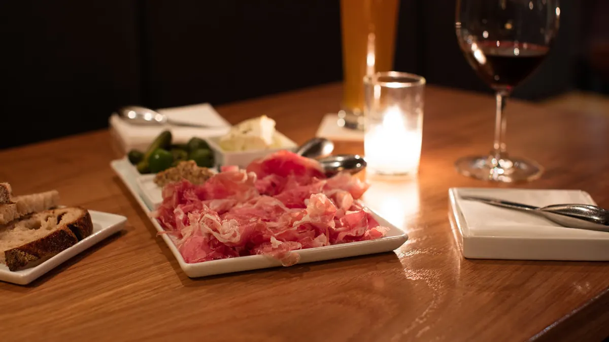 Restauranttafel met ham, brood, een glas rode wijn en een kaarsje