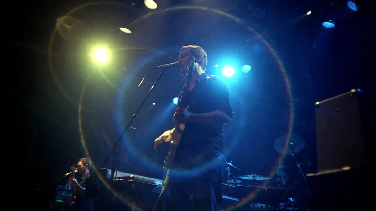 Zanger met gitaar en band op een podium in blauw en wit spotlicht