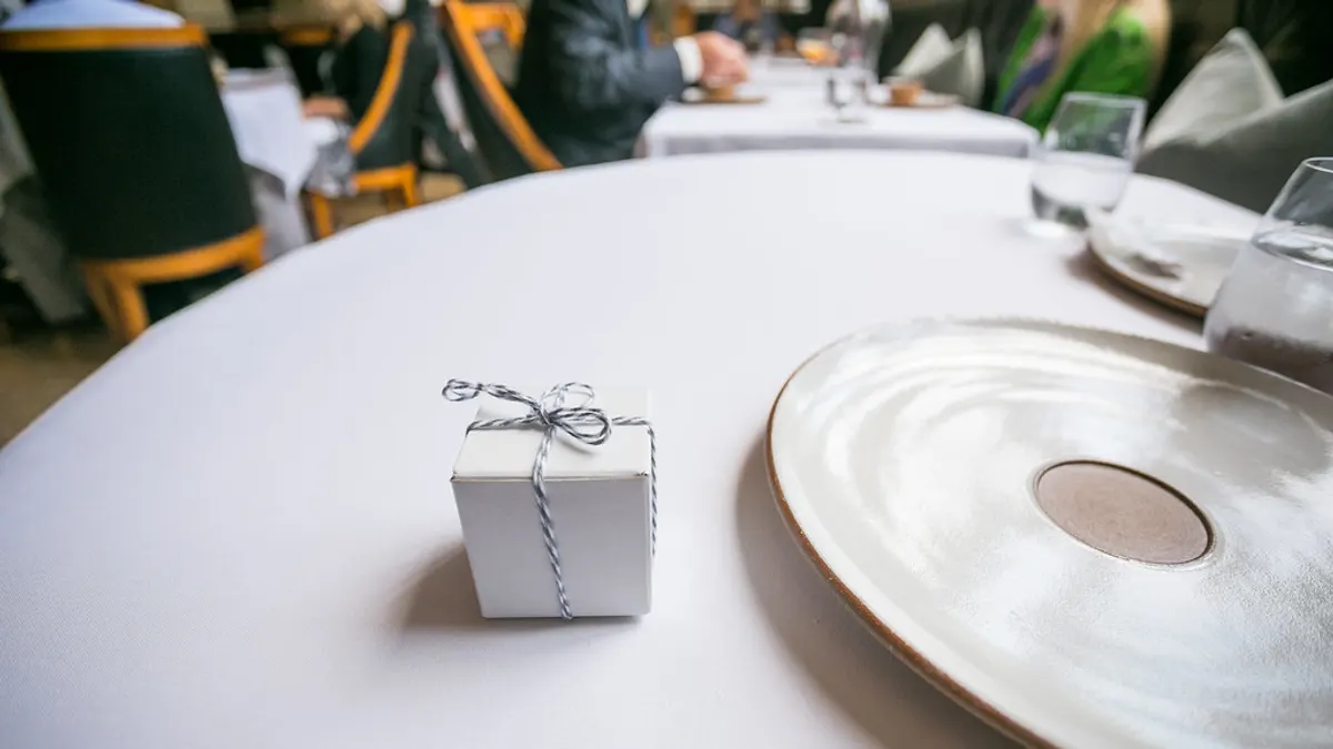 Klein wit doosje met een touwtje als bedankje naast een bord op een feesttafel