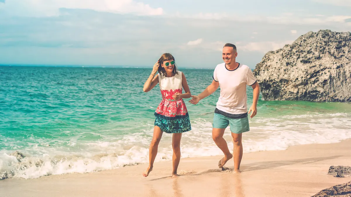 Lachend stel loopt hand in hand over een tropisch strand langs turquoise zee