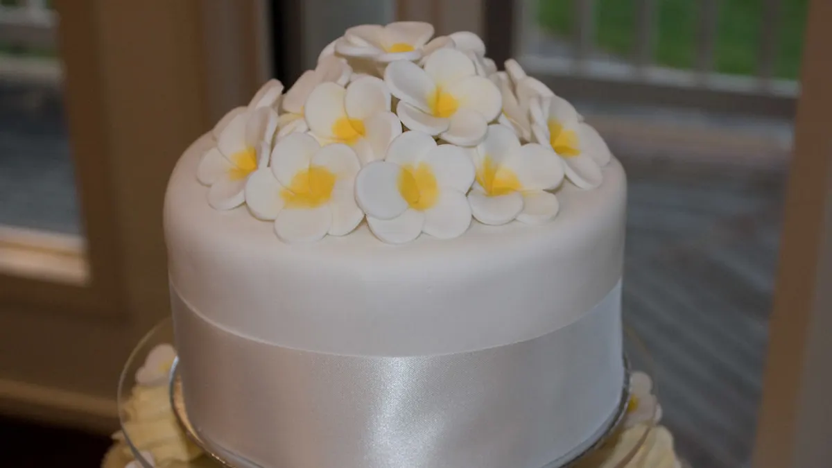 Witte taartlaag strak afgewerkt met gladde fondant, een satijnen lint en suikerbloemen