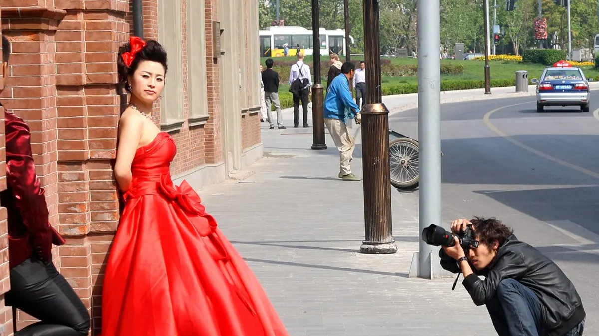 Vrouw in een rode baljurk poseert op straat terwijl een fotograaf neerknielt
