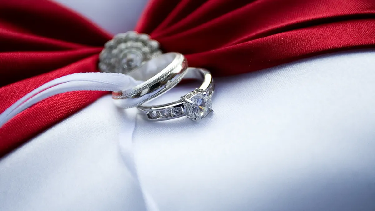 Verlovingsring met diamant en een trouwring op een rood lint en wit kussen