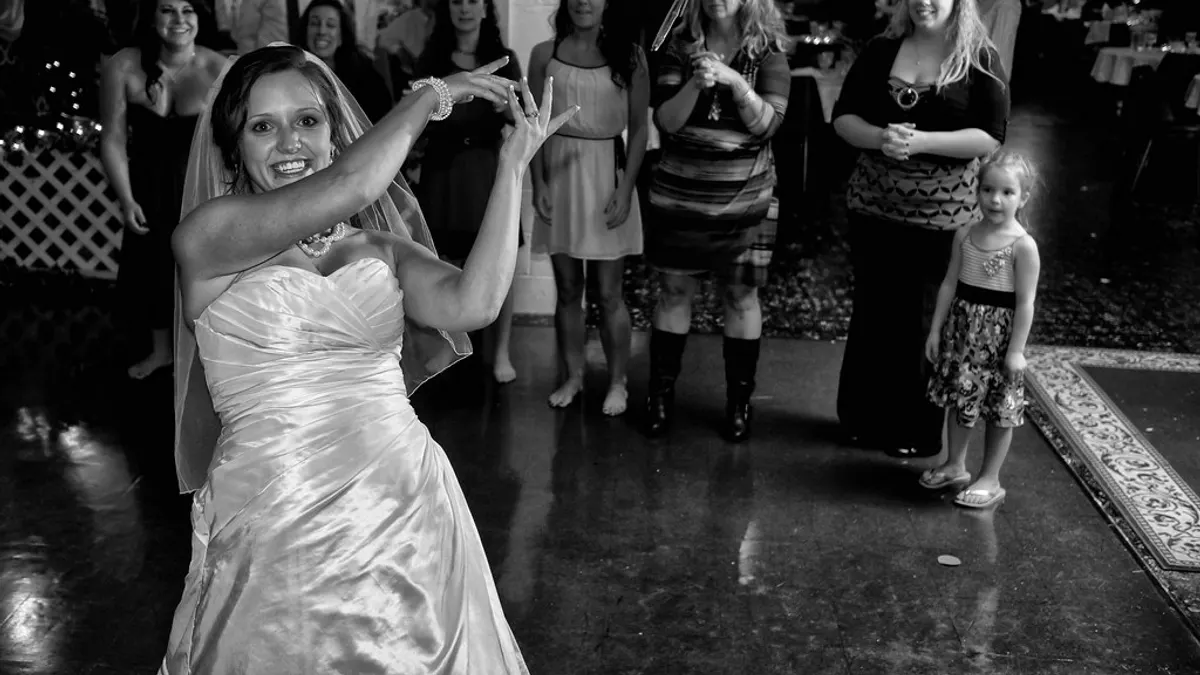Bruid in een satijnen jurk danst uitbundig terwijl gasten toekijken