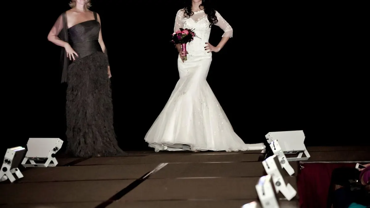 Twee modellen in een zwarte avondjurk en een witte trouwjurk op een catwalk