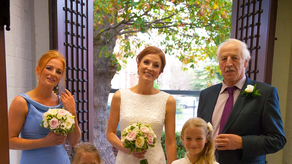 De bruid met haar bruidsmeisje in het blauw en twee bloemenmeisjes bij de ingang van de ceremonie
