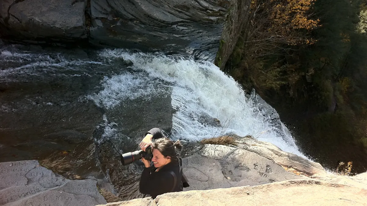 Fotografe met camera zit op een rots naast een waterval