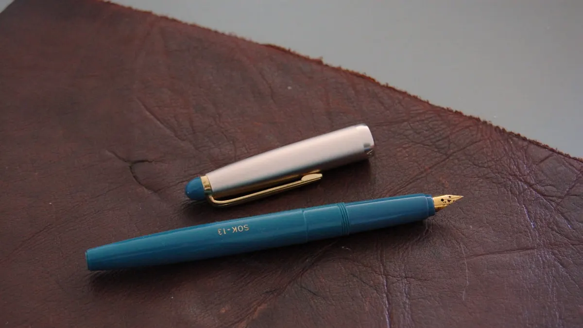 Een blauwe vulpen met afgenomen dop op een stuk donkerbruin leer