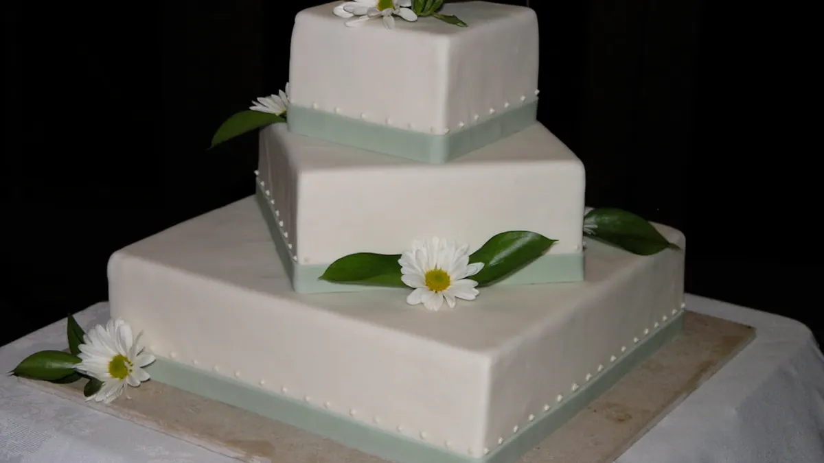 Een cupcaketoren met witte en roze cupcakes en een klein aansnijtaartje bovenop