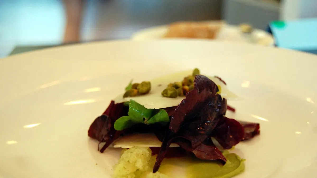 Een vegetarisch voorgerecht met paarse slablaadjes, kaasschaafsel en pistache op een wit bord
