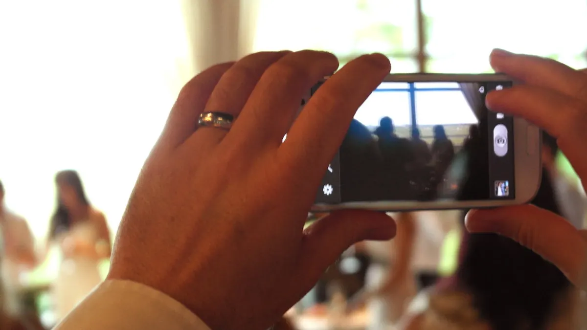Hand met trouwring houdt een smartphone vast om de ceremonie te fotograferen