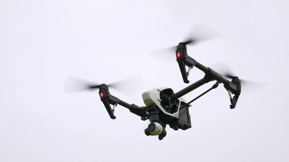 Een cameradrone met draaiende propellers hangt in een bewolkte lucht