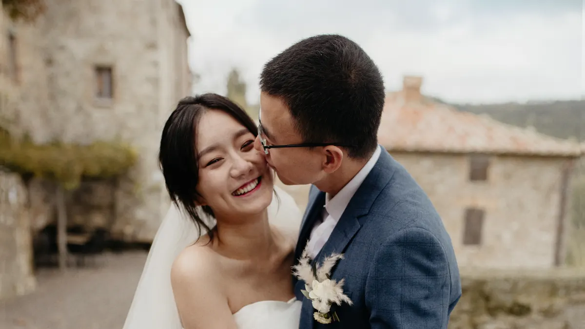 Een lachende bruid krijgt een kus van haar bruidegom voor oude stenen huizen in Toscane