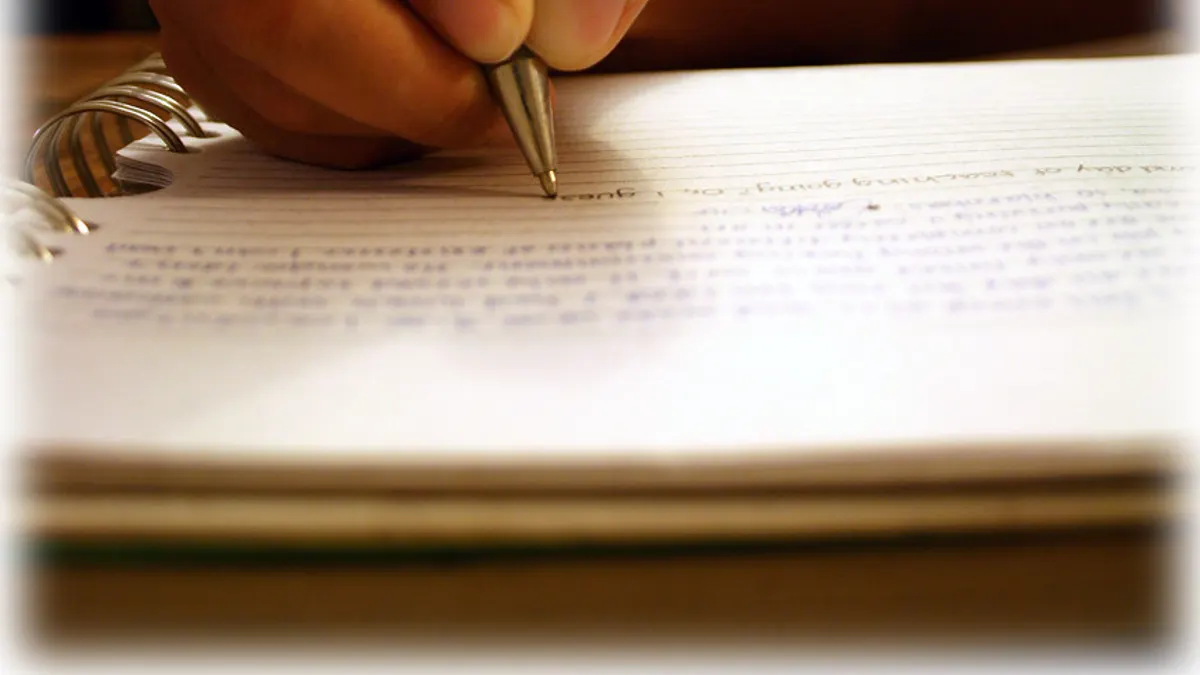 Een hand schrijft met een pen een boodschap op papier