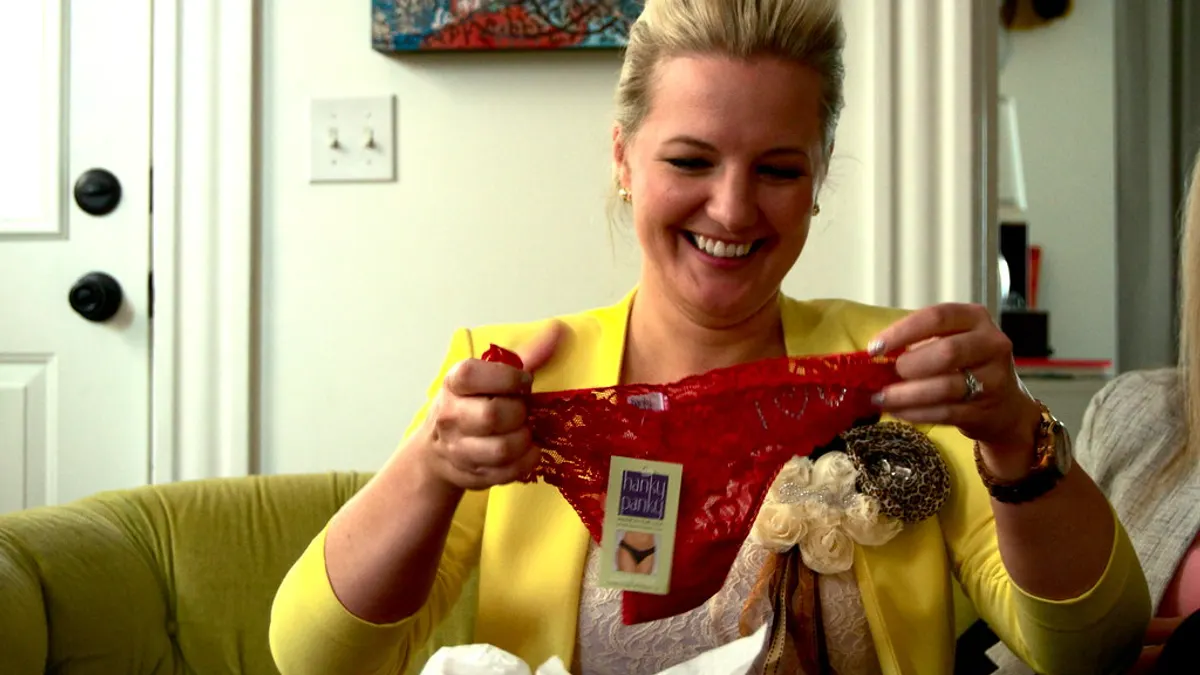 Lachende vrouw in geel jasje houdt een rood cadeautje omhoog dat ze net uitpakte