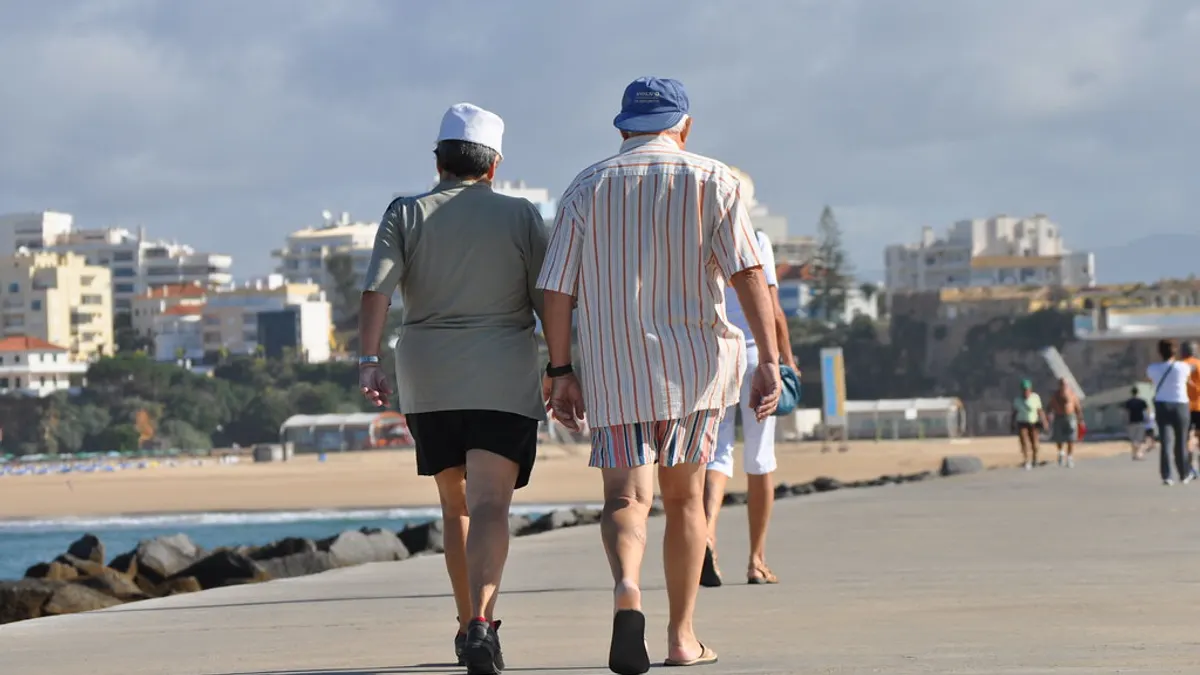 Een ouder koppel wandelt samen over een zonnige boulevard aan zee