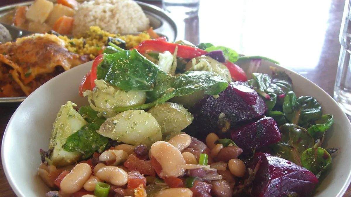 Een kom zelfgemaakte salade met witte bonen, rode biet, aardappel en spinazie naast een bord met rijst en een ovenschotel