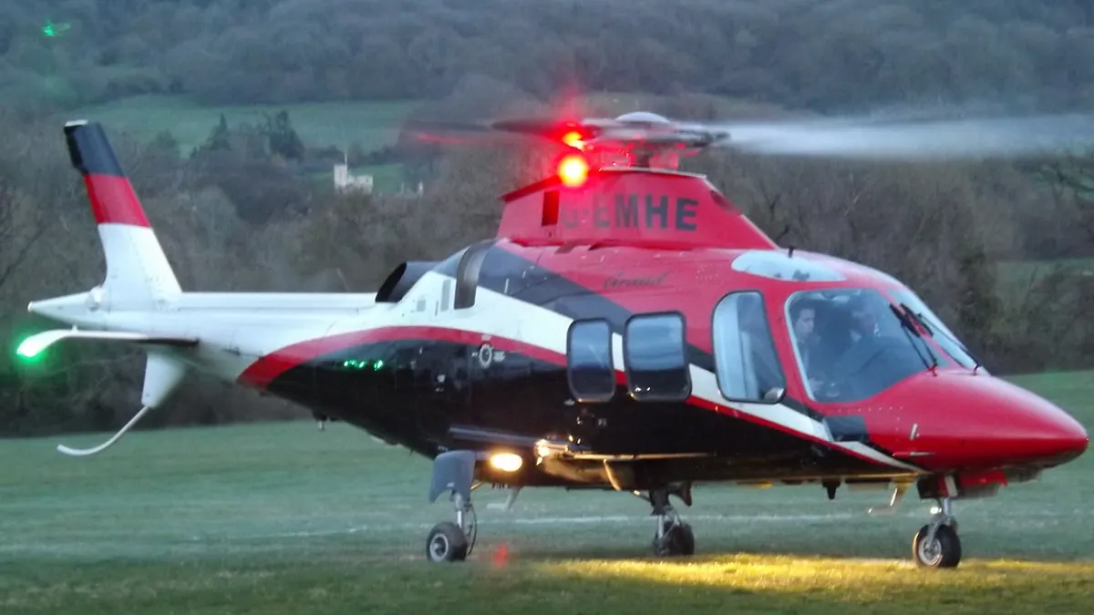 Een rood met witte helikopter staat met draaiende rotor op een grasveld in de schemering
