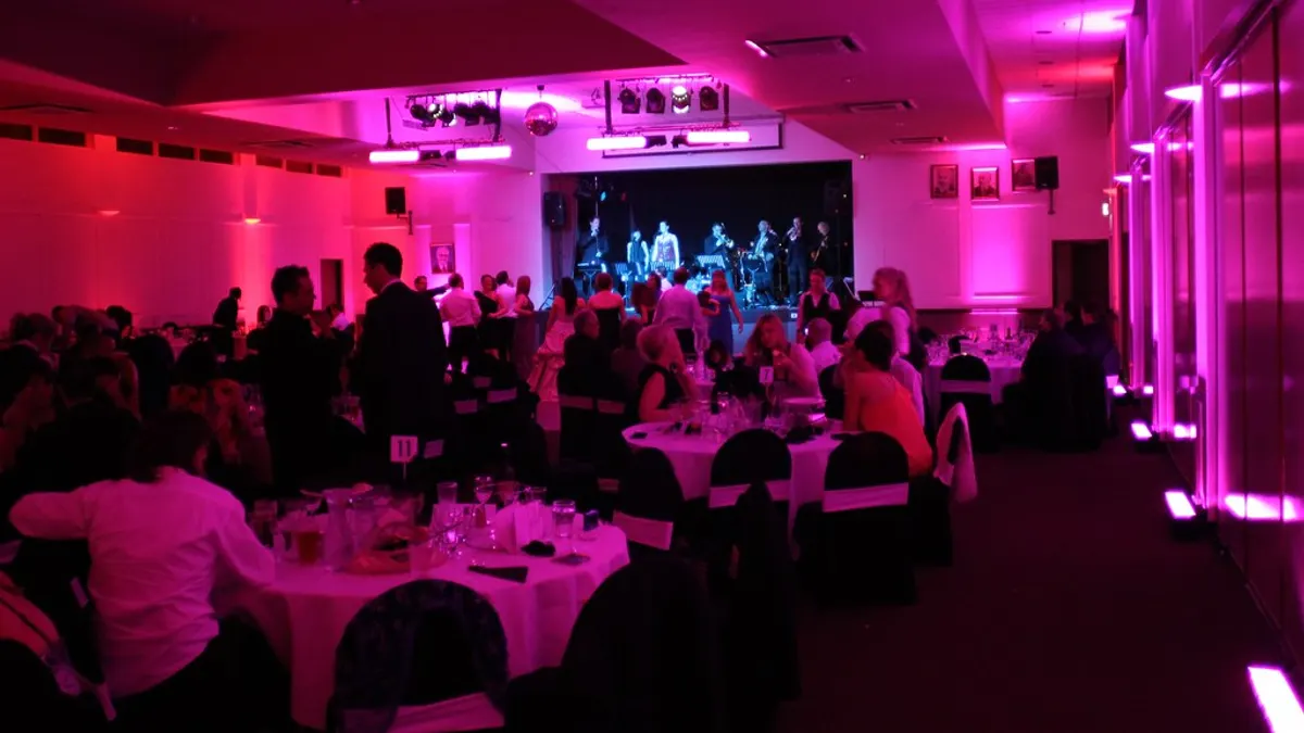 Feestzaal in roze licht met ronde tafels en een band op het podium