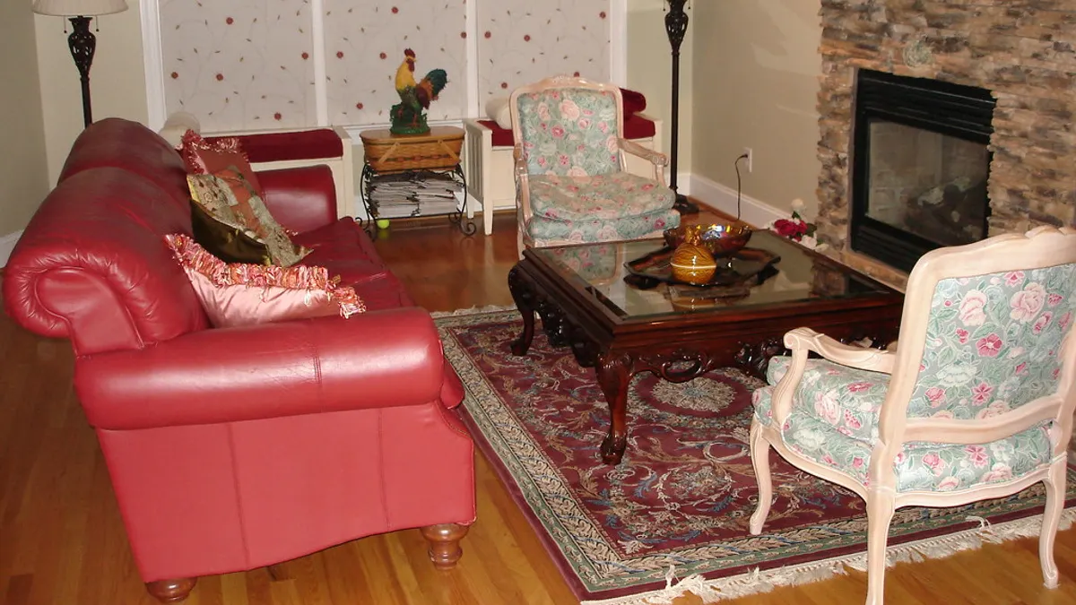 Ingerichte woonkamer met een rode leren bank, twee bloemetjesstoelen en een open haard