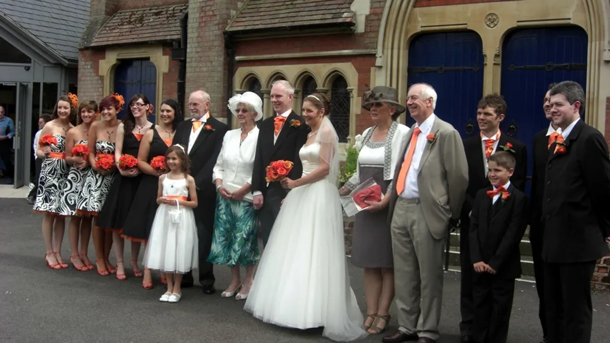 Bruidspaar met familie en bruidsmeisjes met oranje bloemen voor een stenen gebouw