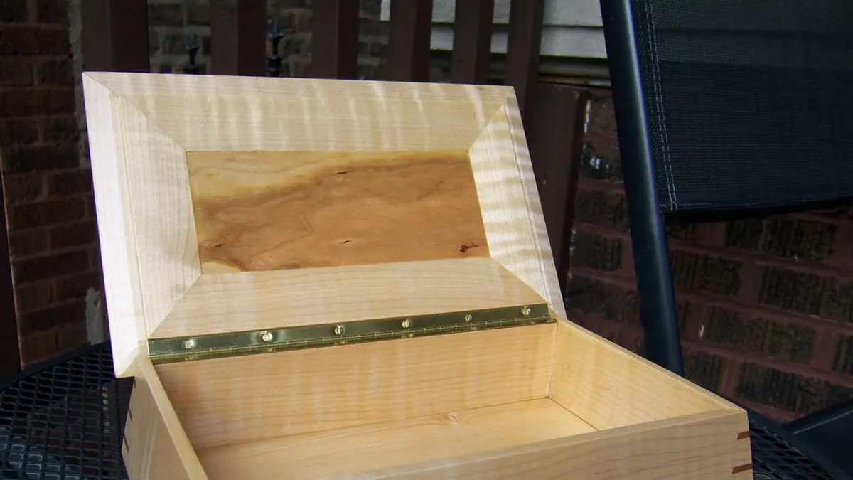 Een open, handgemaakte houten herinneringsdoos met koperen scharnieren op een tuintafel