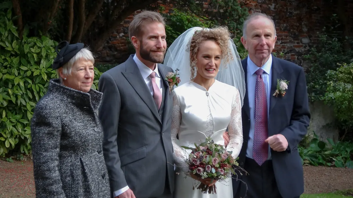 Bruidspaar staat met twee oudere familieleden in een tuin
