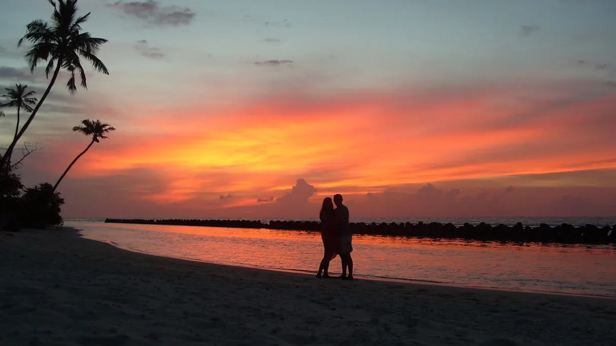 Een koppel staat bij zonsondergang aan het strand tussen de palmbomen