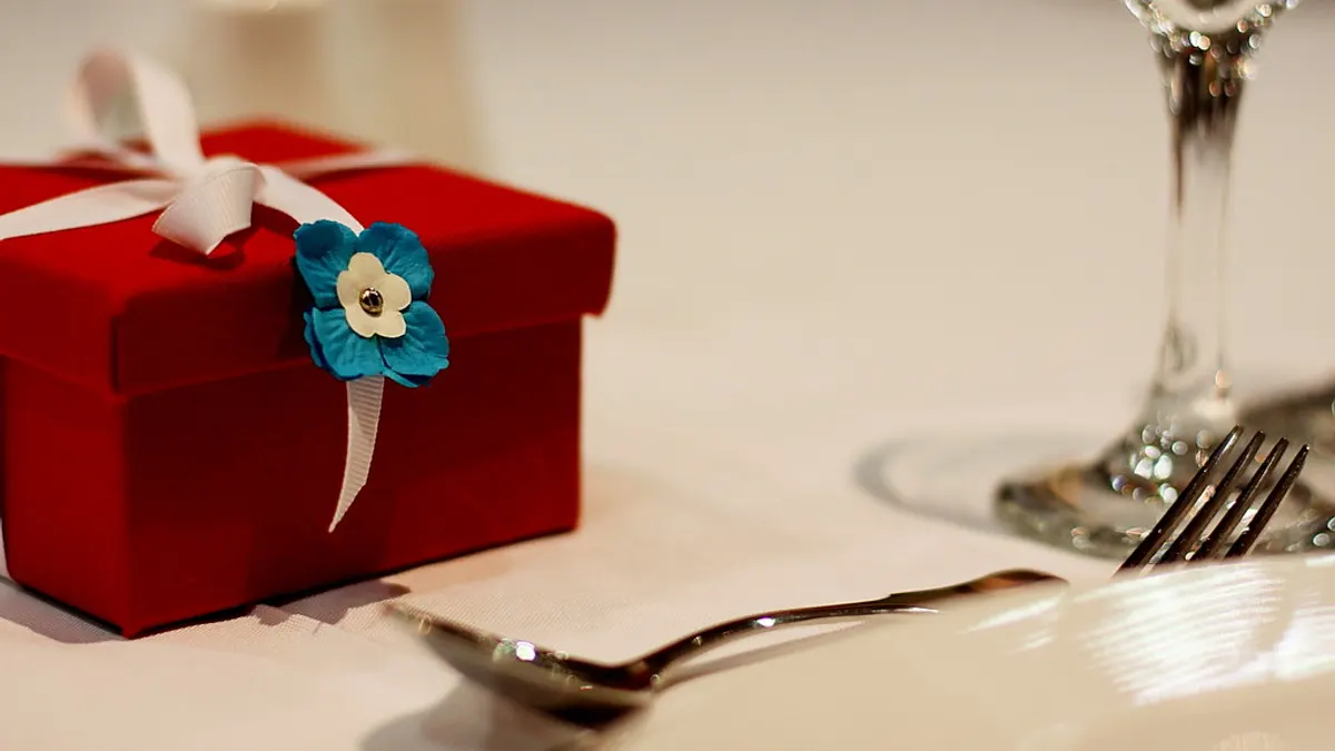 Rood cadeaudoosje met een blauw bloemetje naast een lepel op een gedekte tafel