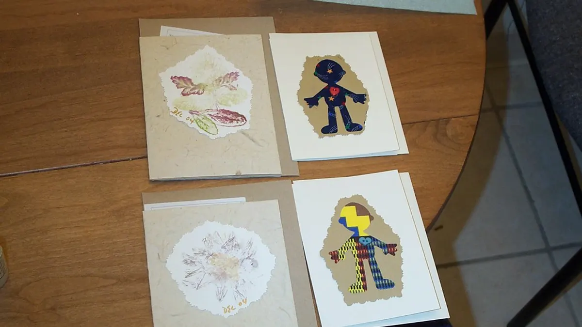 Vier zelfgemaakte kaarten met bladafdrukken en uitgeknipte figuurtjes op een houten tafel