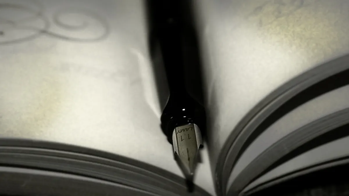Een vulpen met stalen penpunt rust tussen de bladzijden van een opengeslagen schrift met sierlijke krullen
