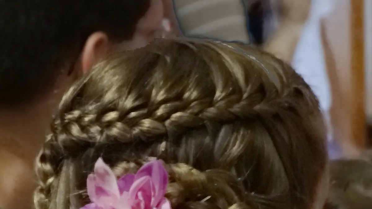Achterhoofd van een meisje met gevlochten haar en een roze bloem in de vlecht
