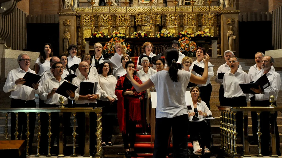 Een koor met dirigente zingt op de trappen voor het altaar van een kerk