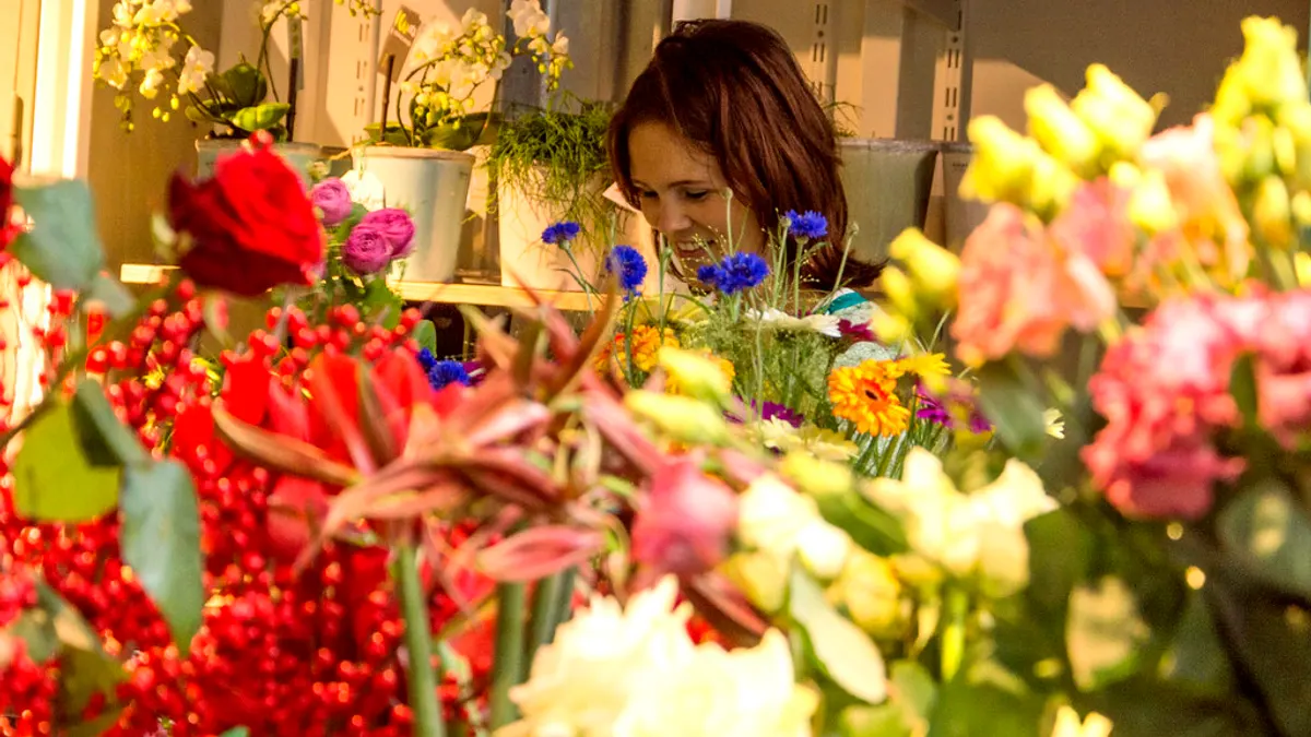 Een bloemist werkt in haar winkel achter emmers vol rozen, korenbloemen, gerbera's en bessen