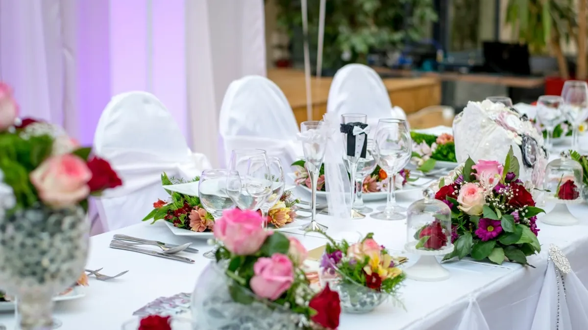 Gedekte dinertafel met witte tafellinnen, glazen en roze bloemstukken, klaar voor het trouwdiner