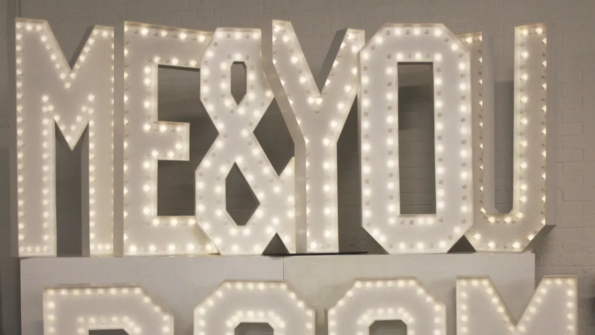 Grote witte lichtletters ME & YOU vol lampjes, opgesteld tegen een bakstenen muur
