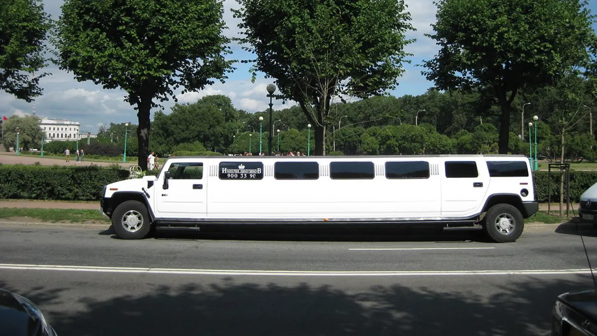 Een witte stretchlimousine op basis van een Hummer rijdt langs een laan met bomen