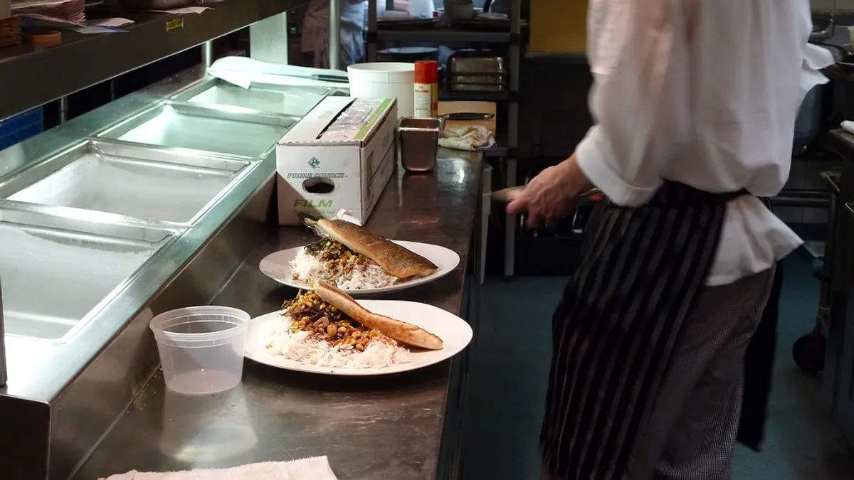 Twee borden met vis en rijst staan klaar aan de doorgeefbalie van een keuken