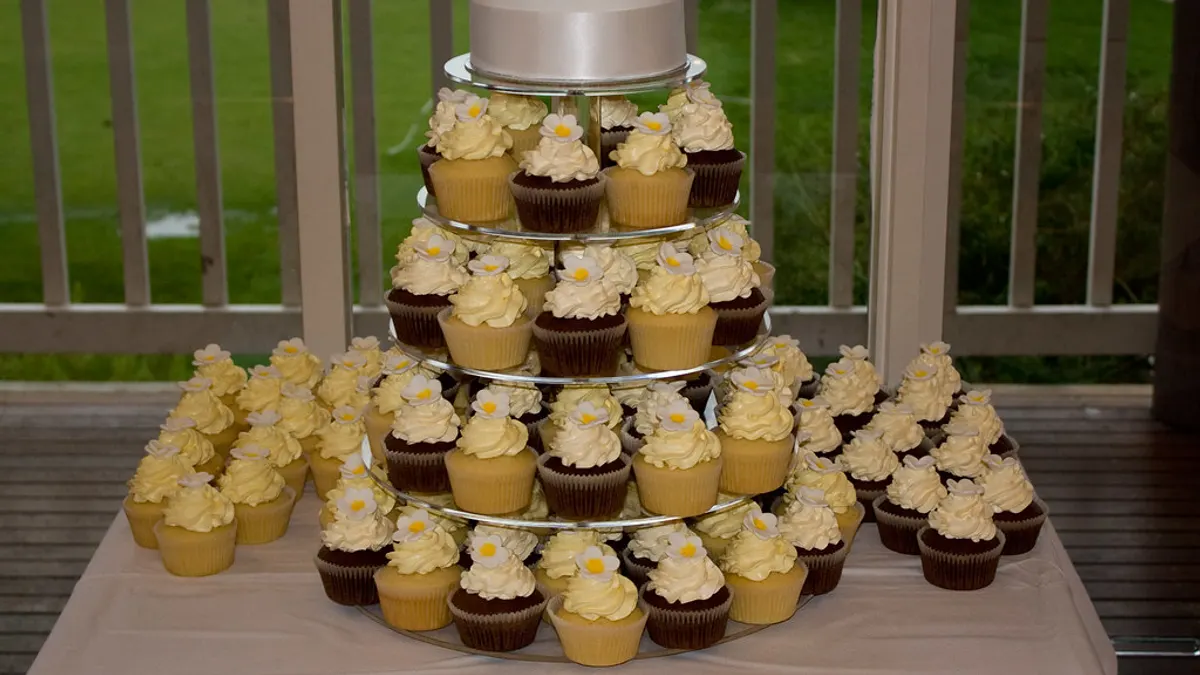 Etagère met cupcakes en bovenaan een kleine witte aansnijtaart op een trouwfeest