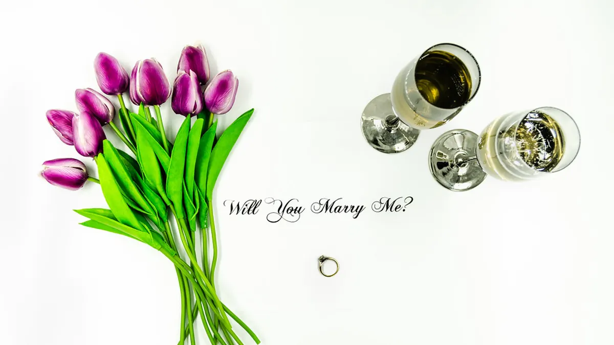 Paarse tulpen, twee glazen champagne en een verlovingsring met de vraag Will You Marry Me