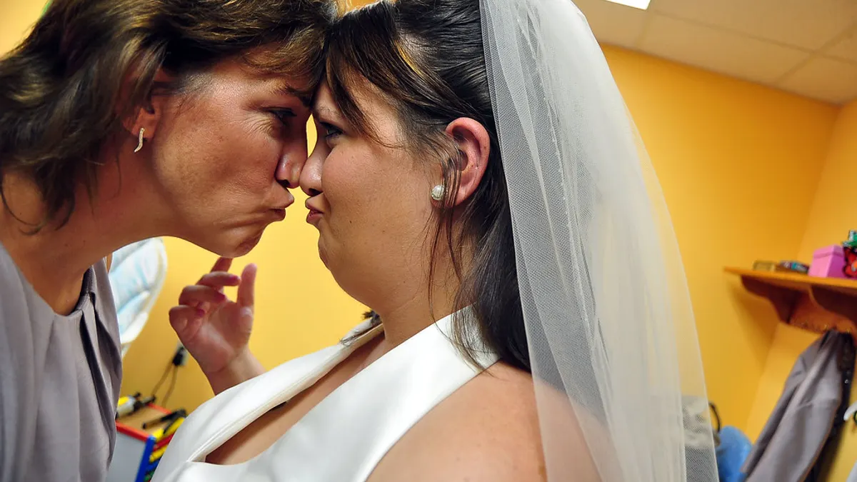 Een moeder drukt haar voorhoofd liefdevol tegen dat van de bruid met sluier