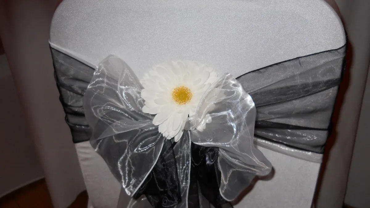 Witte stoelhoes met een strik van zwarte en zilveren organza en een witte gerbera