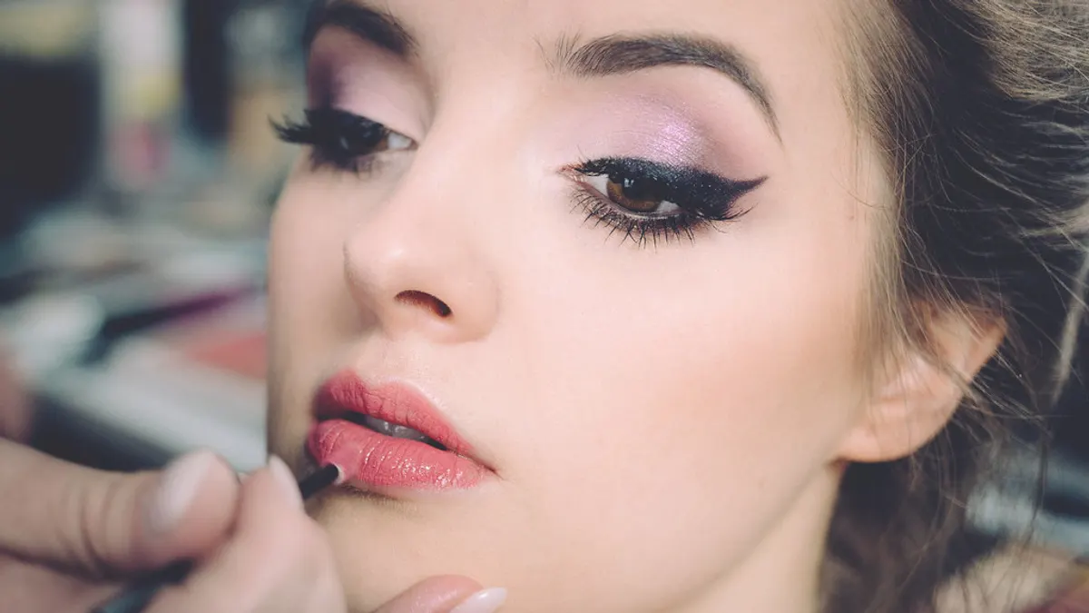 Een visagist brengt met een penseel lippenstift aan op een opgemaakt gezicht