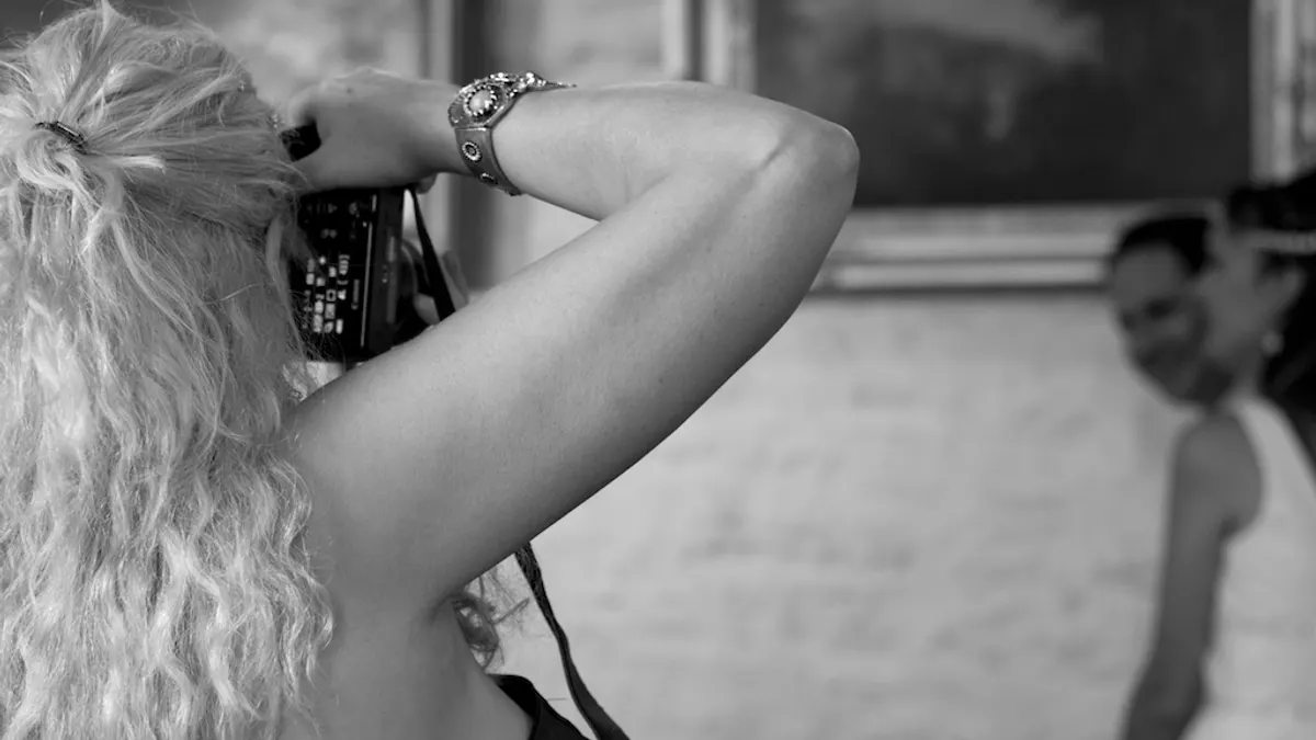 Zwart-witfoto van een gaste die met haar camera de bruid fotografeert tijdens de bruiloft