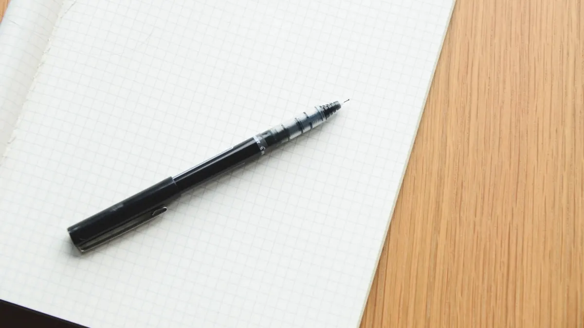 Een leeg ruitjesblad met een zwarte pen op een houten tafel, klaar om de vragen voor het antwoordformulier te noteren