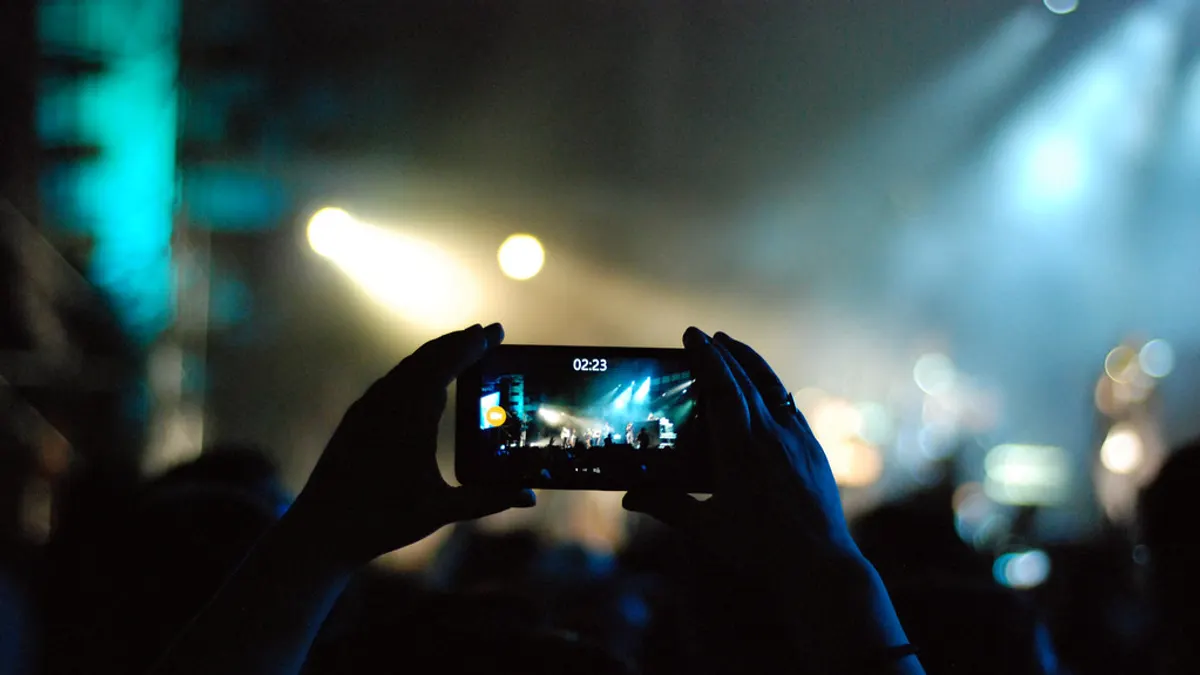 Twee handen houden een smartphone horizontaal vast en filmen in gedempt licht