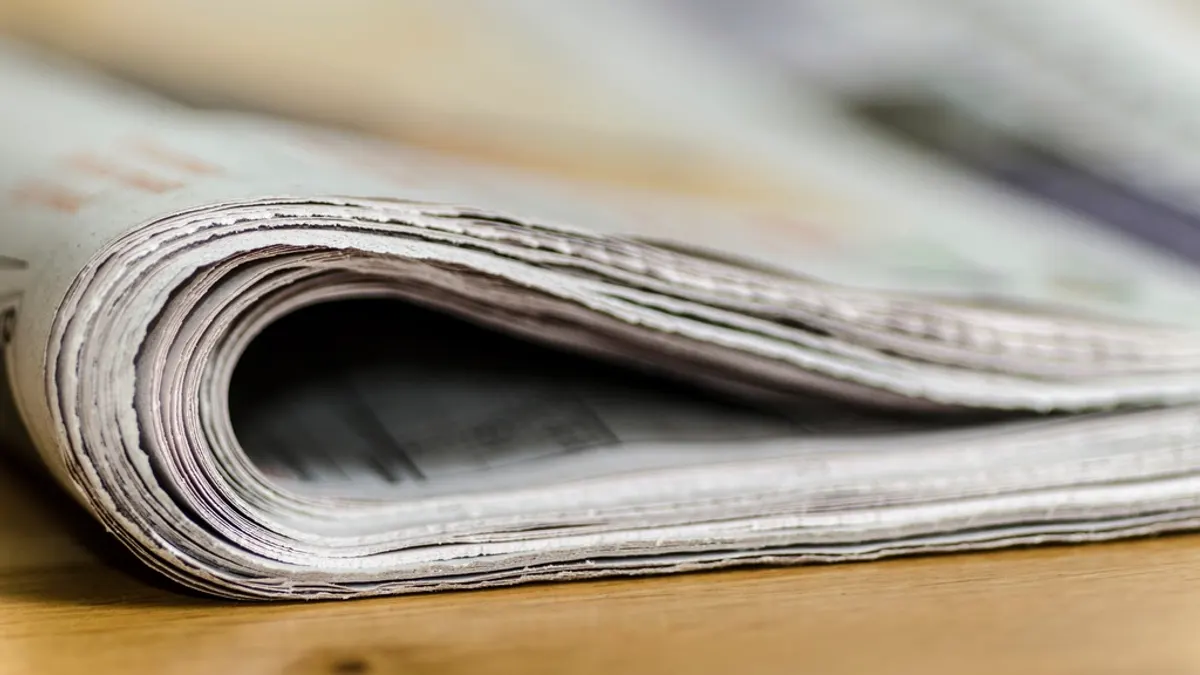 Een dichtgevouwen krant ligt op een houten tafel, van dichtbij gefotografeerd
