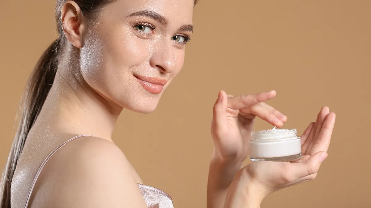 Een vrouw neemt crème uit een potje om haar huid te verzorgen