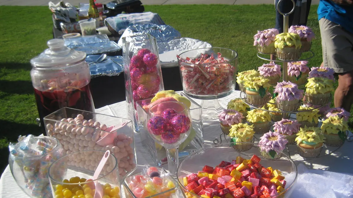Sweet table in de tuin met glazen potten vol snoep en een etagère met bloemcupcakes