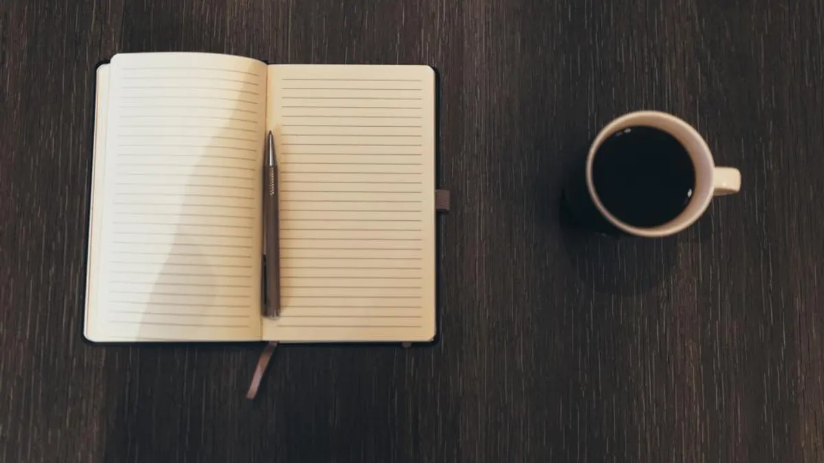 Een opengeslagen notitieboek met een pen naast een kop zwarte koffie op een donkere houten tafel